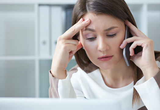 Warried businesswoman talking on phone while working on computer at desk in office.