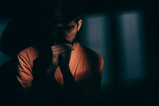 Prisoner man in dark cell depressed or praying