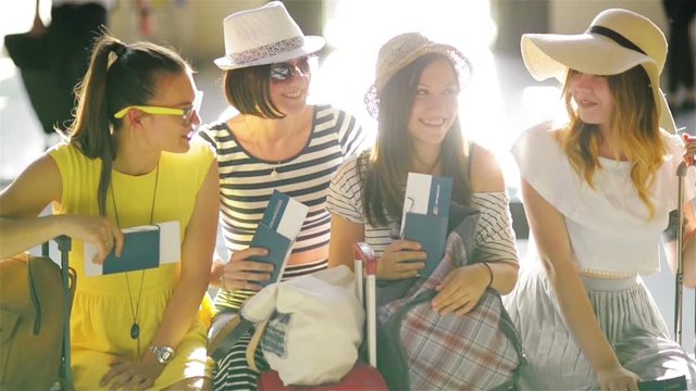 Four Brunettes Wearing Summer Clothing are Sitting in the Waiting Room at the Airport with Passports and Tickets in Hands.