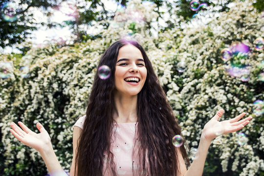The girl smiles with joy against a white wall of flowers, with flying soap bubbles