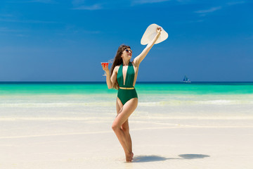Fototapeta na wymiar Beautiful brunette in a straw hat with a martini glass on the shore of a tropical beach. Summer vacation concept.