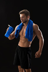 Obraz na płótnie Canvas Vertical studio shot of a handsome young muscular man posing shirtless on black background holding shaker bottle training exercising workout sportsman athlete active healthy lifestyle.