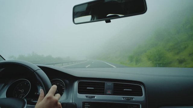 Close up of patient, sensible and cautious young driver turning on the fog headlights while driving through mist and murk covered highway with low to none visibility, moody and atmospheric adventures