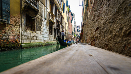 Venetian gondolier punting gondola through green canal waters of Venice Italy.Picture with blurry timber on the foreground.