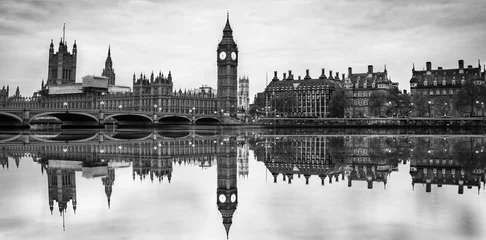 Gordijnen Dramatic, vintage black and white picture of Big Ben and Westminster bridge in London at dusk with blurry reflection in Thames river. © offcaania