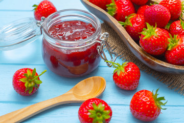 Jar of strawberry jam on blue wooden background