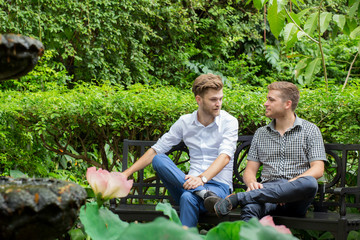 Naklejka na ściany i meble Two friends men talking sitting in a garden.