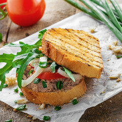 Grilled sandwich with tuna salad, tomato, onion and arugula on a wooden table. Diet healthy finger food made of toasts, vegetables and fish.