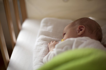Newborn baby in crib with nipple in mouth