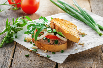 Fish sandwich made of grilled toast, tuna salad and vegetables on a rustic wooden table. Delicious healthy diet meal.