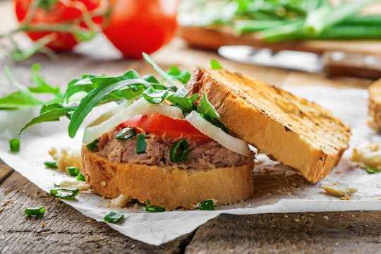 Grilled sandwich with tuna salad, tomato, onion and arugula on a wooden table. Diet healthy finger food made of toasts, vegetables and fish.