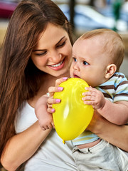 Fototapeta na wymiar First birthday ideas. Happy mother and her baby boy play with balloon outdoors in summer park. Selection of toys for small child.