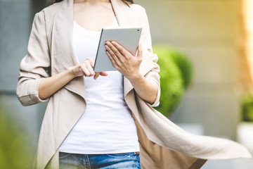 Beautiful Business Woman using digital tablet. Close-up. Beautiful woman in jeans enjoying sunny morning in the city, browsing Internet and drinking coffee. Lens Flare.