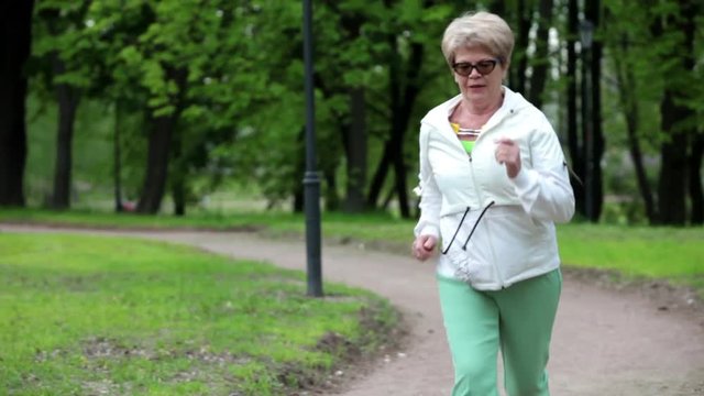 Elder European woman running on the park pathway alone in summer season