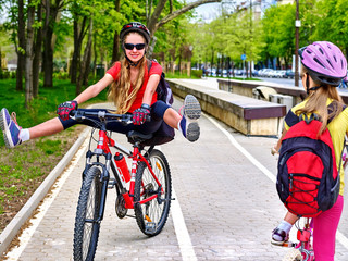 Fototapeta premium Bicycle path with children in city. Girls wearing helmet with rucksack ciclyng ride. Kids on white bike lane . Alternative to urban transport. Oncoming traffic. Children learn new tricks on bike.