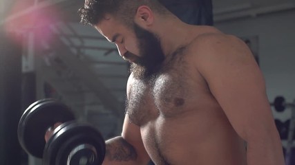 Bodybuilder in training in the gym. Young man doing biceps exercise with dumbbells. Slow motion