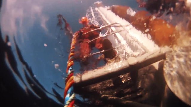 Point of view scooba diver with help of assistant in orange clothes and hard hat pulling colorfull ropes to get out water to surface of sea oil production platform, sunny day