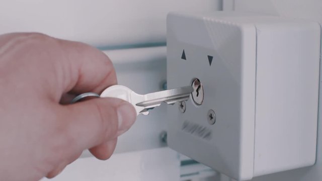 Unrecognizable woman hand put metal key into keyhole of white box with printed arrows on wall, close up