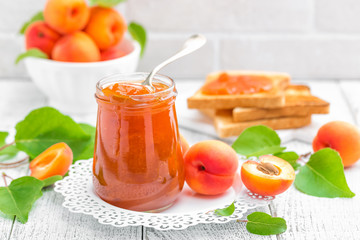 Apricot jam in a jar and fresh fruits with leaves on white wooden table, breakfast
