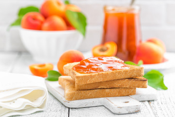 Toasts of bread with apricot jam and fresh fruit with leaves on white wooden table. Tasty breakfast.