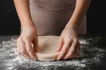 Female hands making dough for pizza on black table