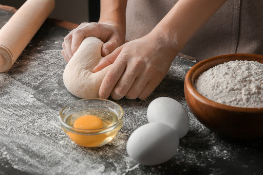 Female hands making dough for pizza on black table