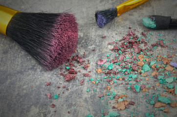A mixture of eye shadows and applicators crumbled on a rustic steel table. Confusing jumble of...