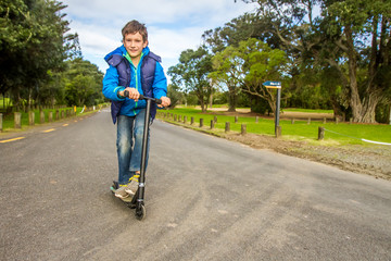 outdoor portrait of young happy preteen boy riding a scooter on natural background