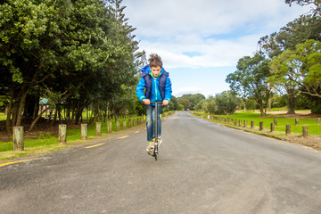 outdoor portrait of young happy preteen boy riding a scooter on natural background