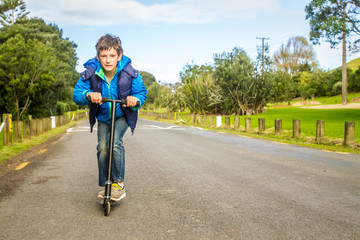 outdoor portrait of young happy preteen boy riding a scooter on natural background