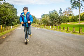 Fototapeta premium outdoor portrait of young happy preteen boy riding a scooter on natural background