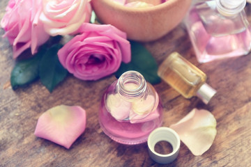 Essential oils with rose petals on wooden background