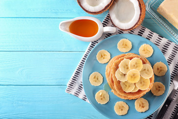 Stack of delicious coconut pancakes with sweet sauce and sliced banana on table