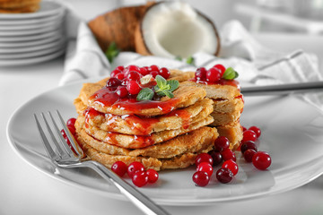 Sliced stack of delicious coconut pancakes with sweet sauce, berries and mint on white table