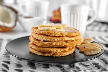 Stack of delicious coconut pancakes with sweet sauce and sliced banana on napkin
