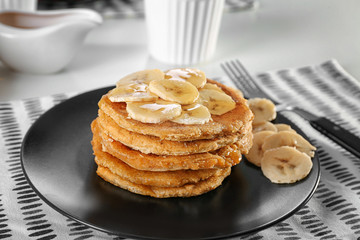 Stack of delicious coconut pancakes with sweet sauce and sliced banana on plate, close up