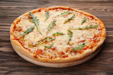 Delicious pizza with melted cheese and rocket salad on wooden table