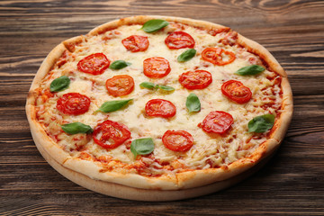 Delicious pizza with tomatoes, basil and melted cheese on wooden background