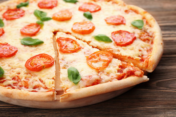 Delicious sliced pizza with tomatoes, basil and melted cheese on wooden background