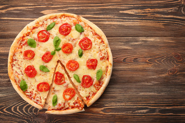 Delicious sliced pizza with tomatoes, basil and melted cheese on wooden background