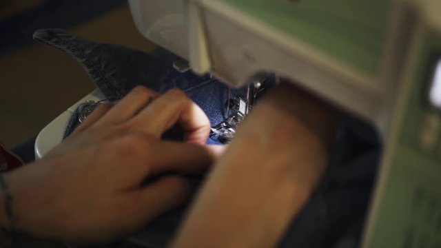 Female hands with tattoos using sewing machine to stitch patch to blue denim jacket, close up slow motion
