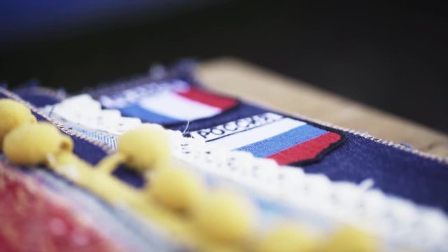 Patterned piece of cloth material with pom poms on denim patches at tailor workshop desk, close up slow motion