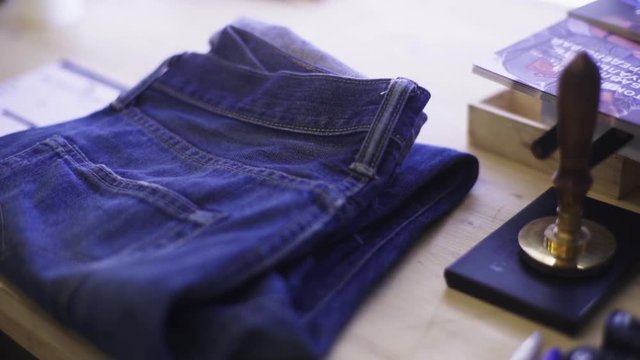 Folded blue denim jeans lean on wooden table desk with leaflets and hand seal stamp press, close up