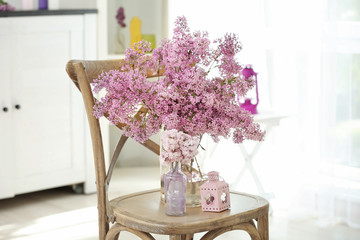 Glass vases with beautiful lilac flowers on chair
