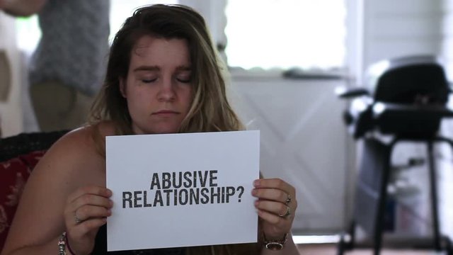 Portrait of abused frazzled girlfriend holding up a sign reading abusive relationship