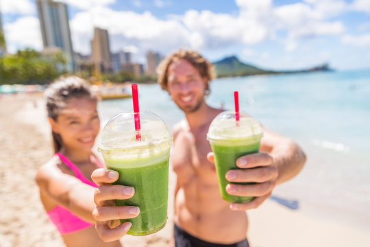 Fitness couple drinking green smoothie at beach. Man and woman holding vegetable smoothies after running sport fitness training. Healthy clean eating lifestyle concept.