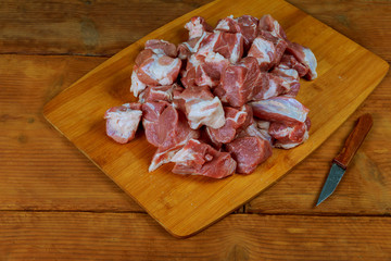 Small peices of crude beef meat with knife on a kitchen board.