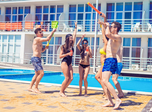 pool party with friends. Group of cheerful young people looking happy dancing at swimming pool together. Guys have water pistols in hands