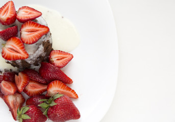 Delicious homemade chocolate cake with fresh red strawberries and cream sauce on white plate.
