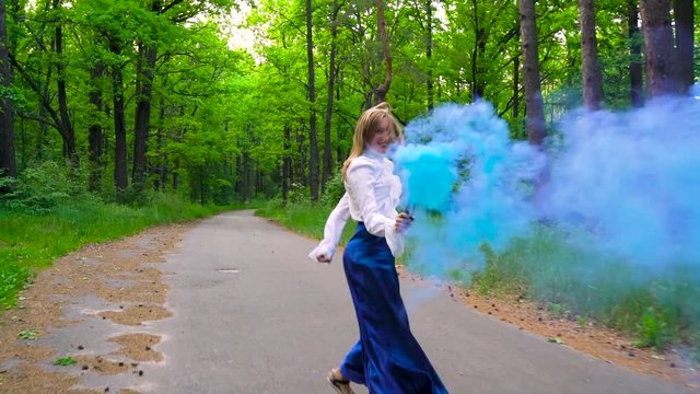 Woman in beautiful clothes runs through the forest waving colored smoke, slow motion
